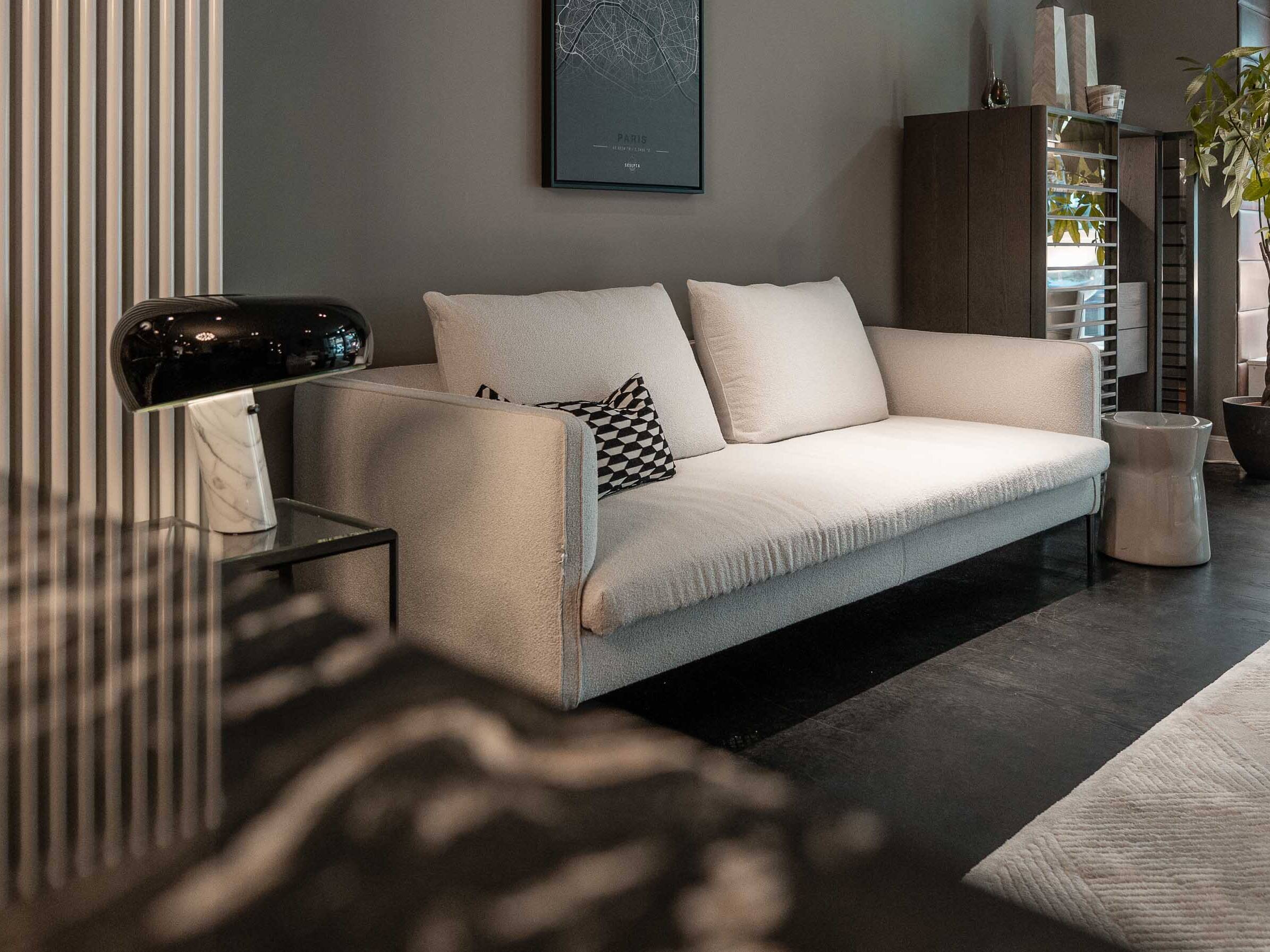Helles Sofa mit gemustertem Kissen und schwarzer Tischleuchte auf Marmorfuß im Showroom Oberkassel