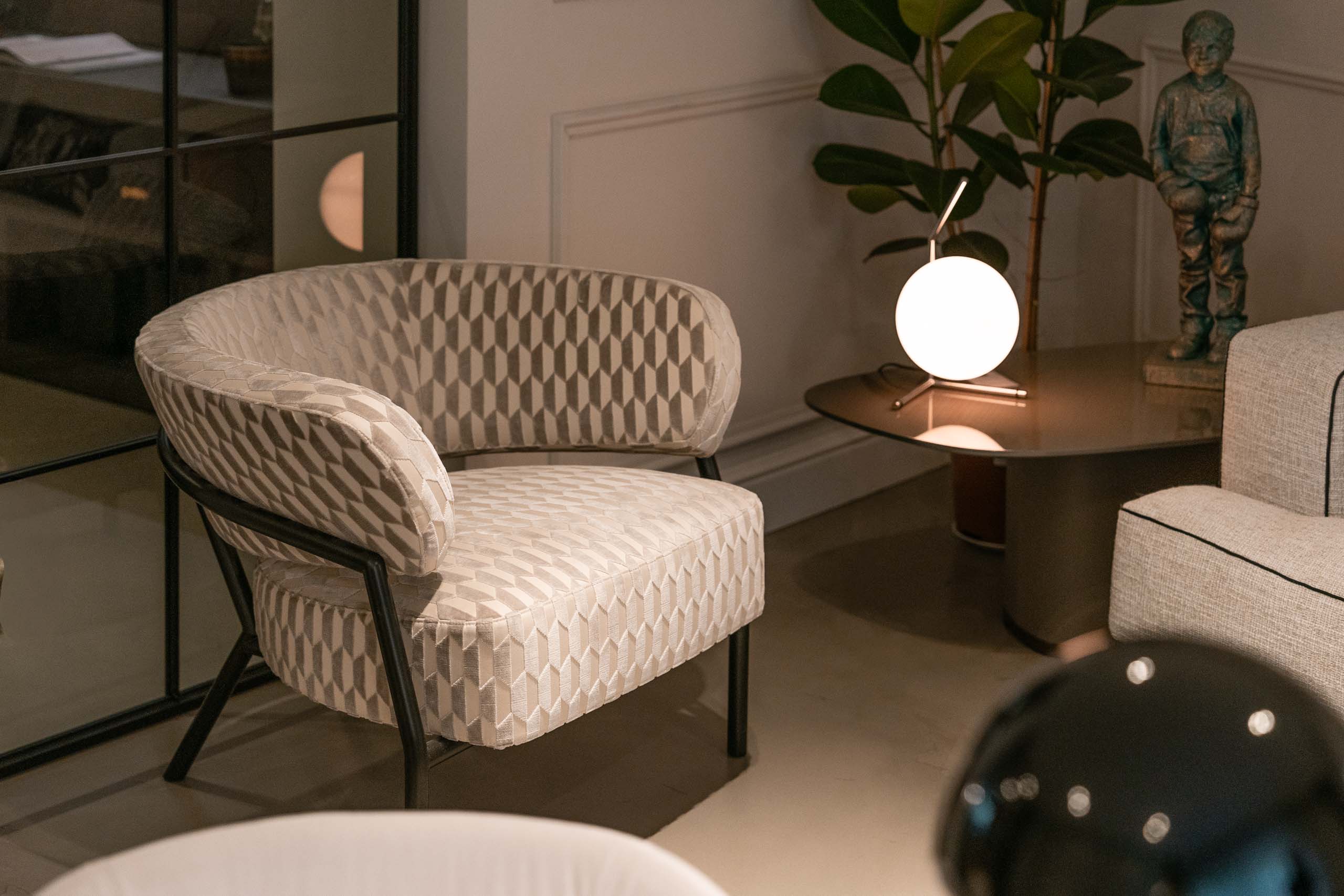 Sessel mit grafisch gemustertem Bezug und Tischleuchte mit Glaskugel im Showroom Oberkassel